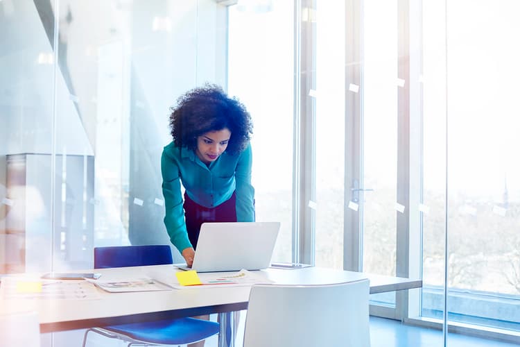 Woman leaning over a desk, looking at a laptop Woman leaning over a desk, looking at a laptop