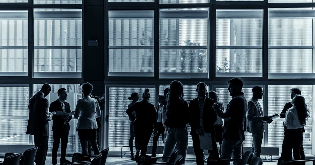 A Group of People in Silhouette in Front of Office Windows at a Conference Representing the Iowa Broker Tour