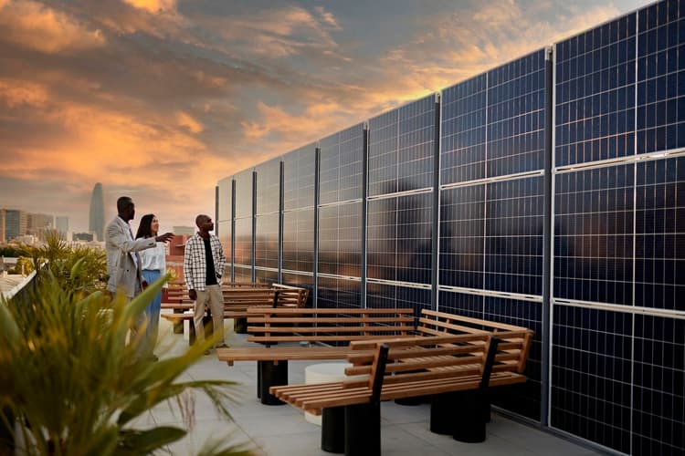 Real estate agent and couple standing on rooftop of environmentally aware office building admiring solar panel system at sunset.