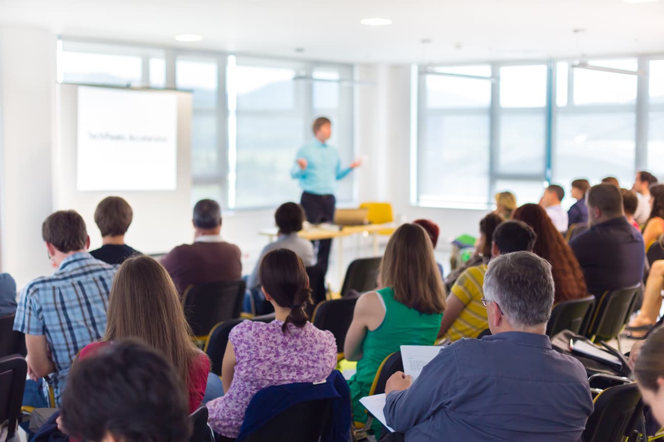A conference speaker giving a presentation in a bright conference room with an audience.