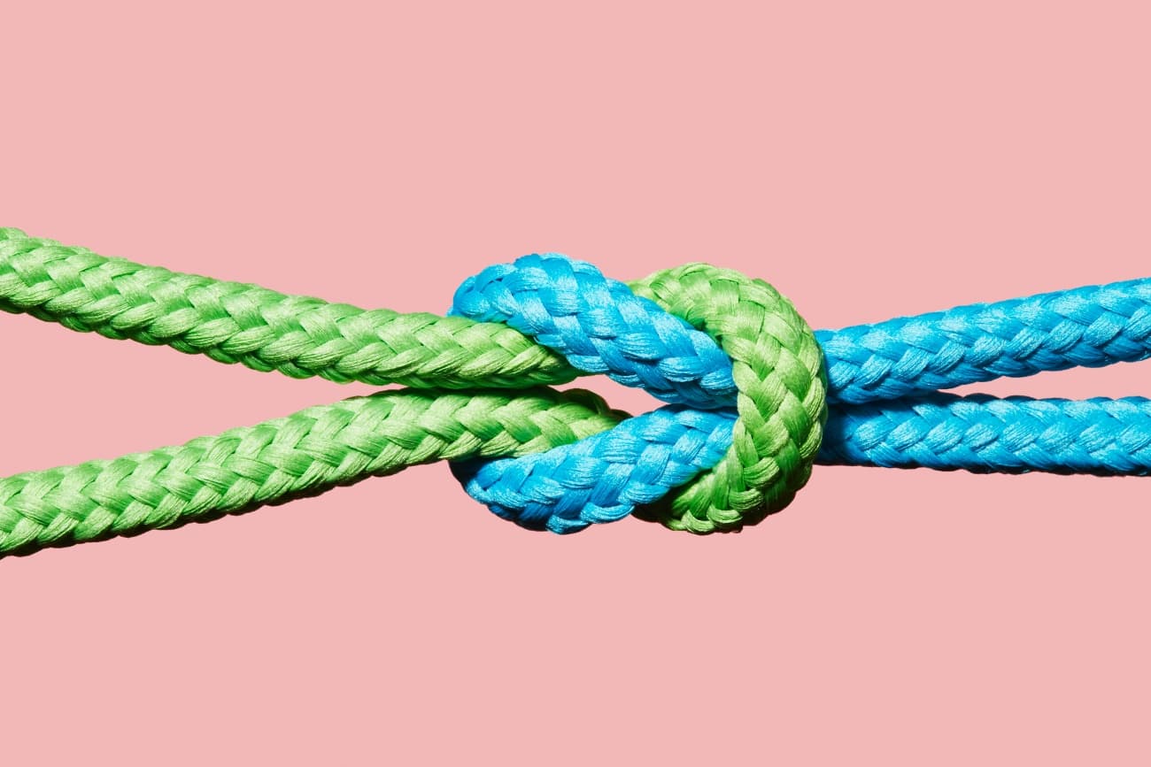 Two colored ropes knotted together on pink background