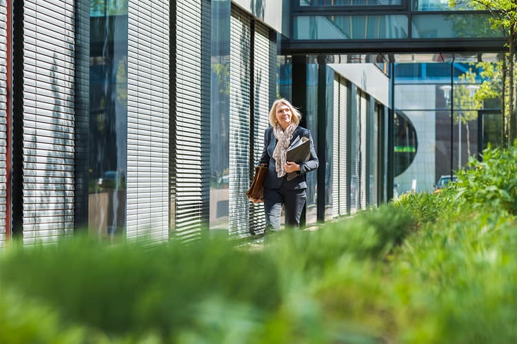 Professional woman walking between an office building and a garden Professional woman walking between an office building and a garden