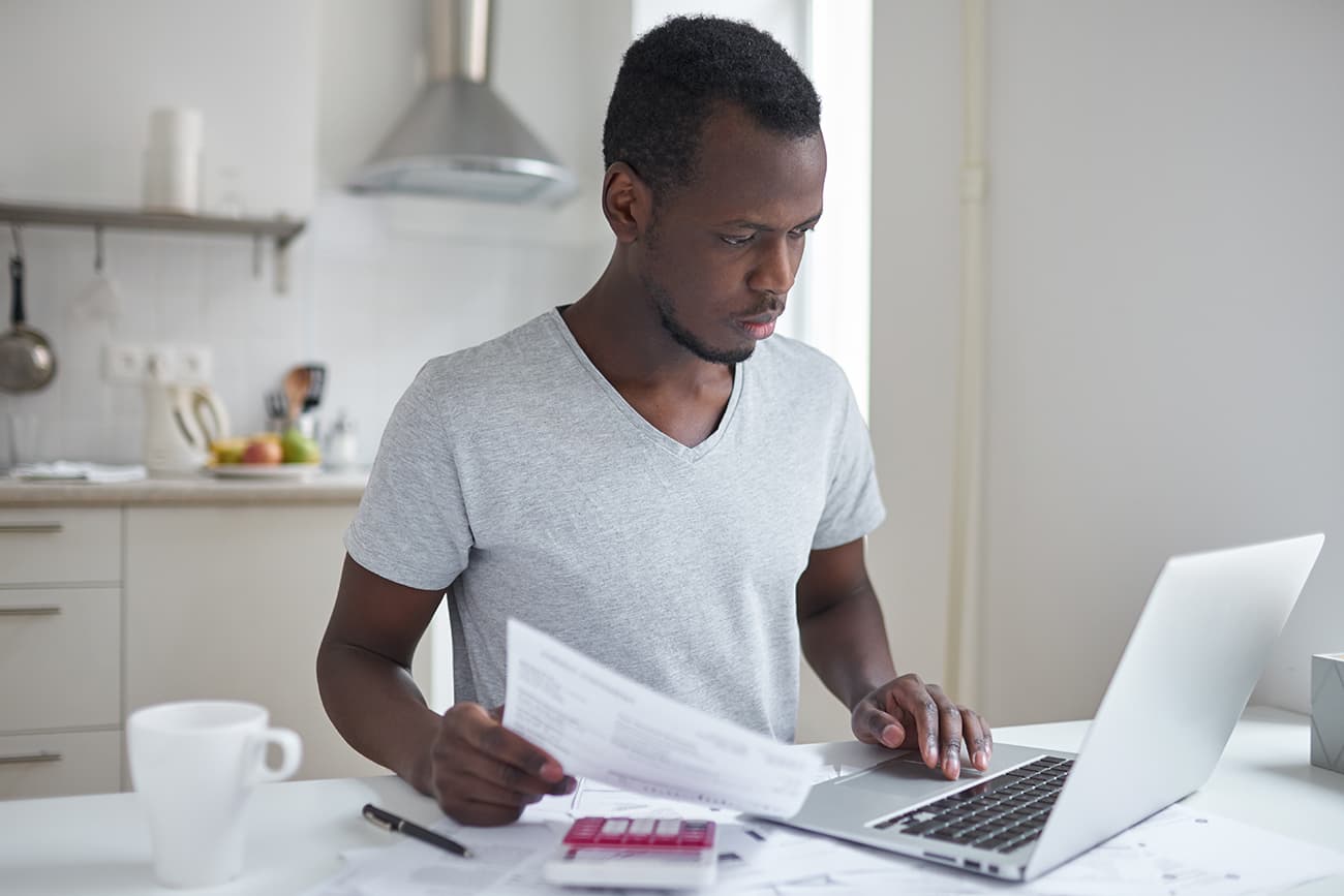 Serious young man at laptop, with papers, calculator