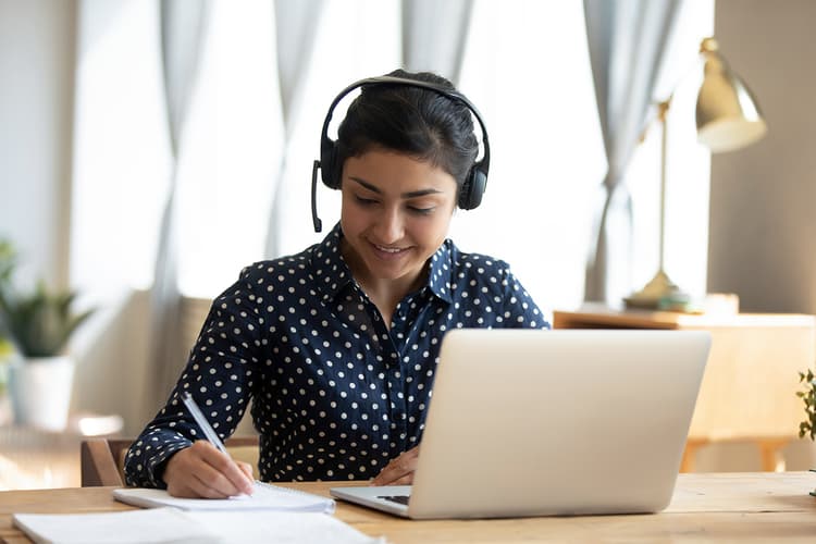 Woman at a laptop, wearing headphones and taking notes Woman at a laptop, wearing headphones and taking notes