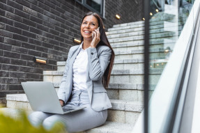 Businesswoman sitting on steps with laptop talking on phone