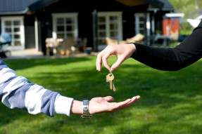 Hands exchanging house keys with home in background
