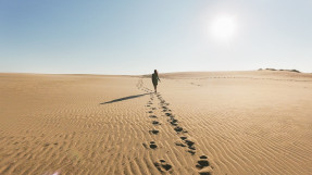 Woman Walking In Desert Against Clear Sky with Footprints in sand