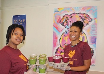 Cups of Goodness juice bar employees carrying trays of fresh juice