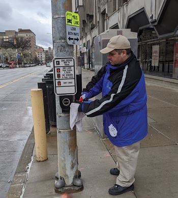 Oakland BID disinfecting the main street crossing signal buttons