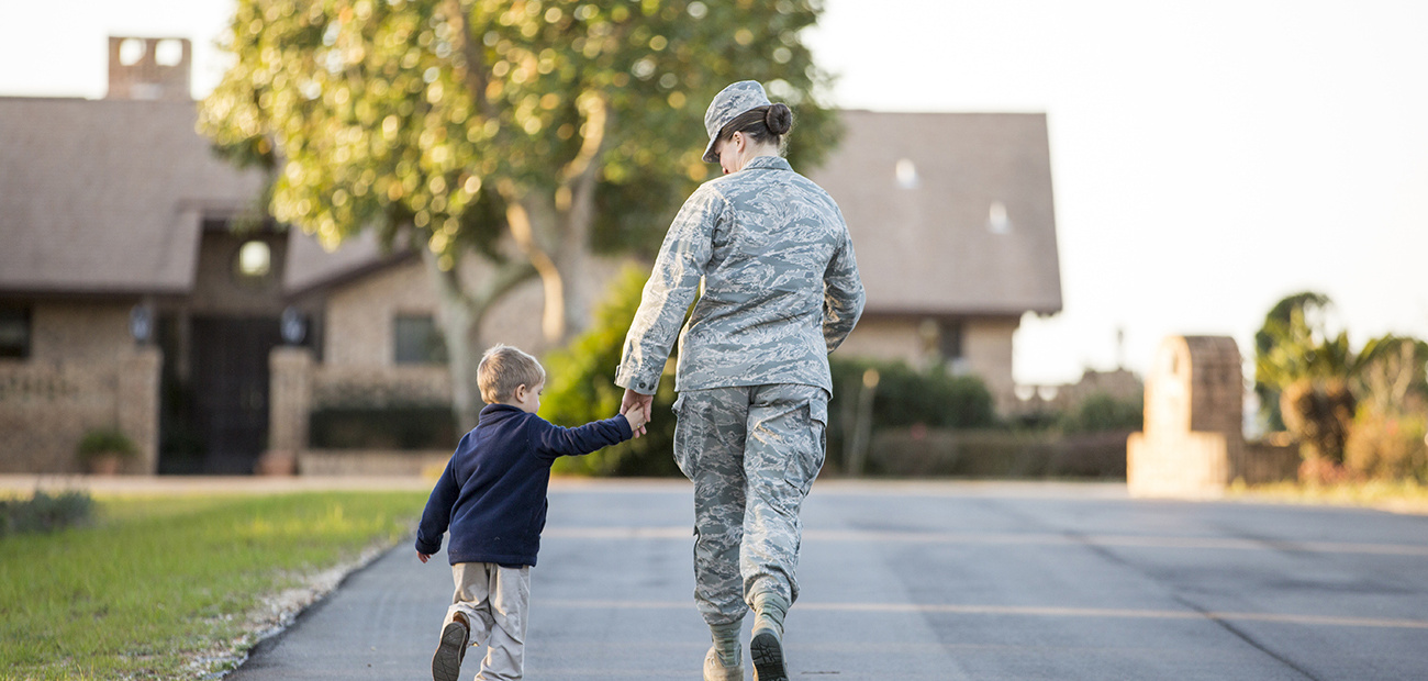 Woman in military fatigues and child walking toward house