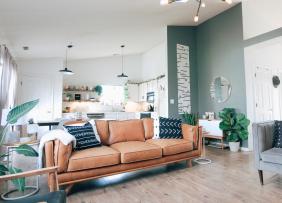 A teal and white living room with ash wood floor, light tan leather couch, and grey love seat.