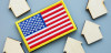 A picture of wooden house-icon pieces surrounding an embroidered American flag patch.