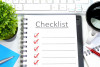 Checklist on a note book, coffee mug, pen and plant on an office desk.