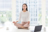 Woman meditating in bright room by laptop